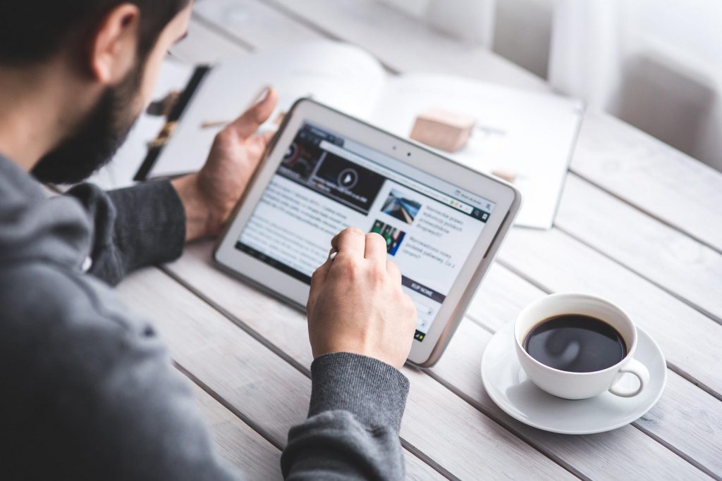AGB – Person, die ein Tablet mit einem Bericht liest, daneben eine Tasse Kaffee, symbolisch für die Durchsicht von Geschäftsbedingungen.