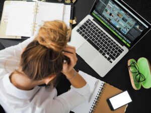 Frau vor dem Laptop arbeitend, hält sich den Kopf