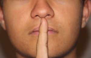 a person signalling "quiet, please" pointing with his finger on his lips