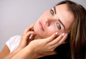 A woman holding her tender juvenile glowing face with her hands
